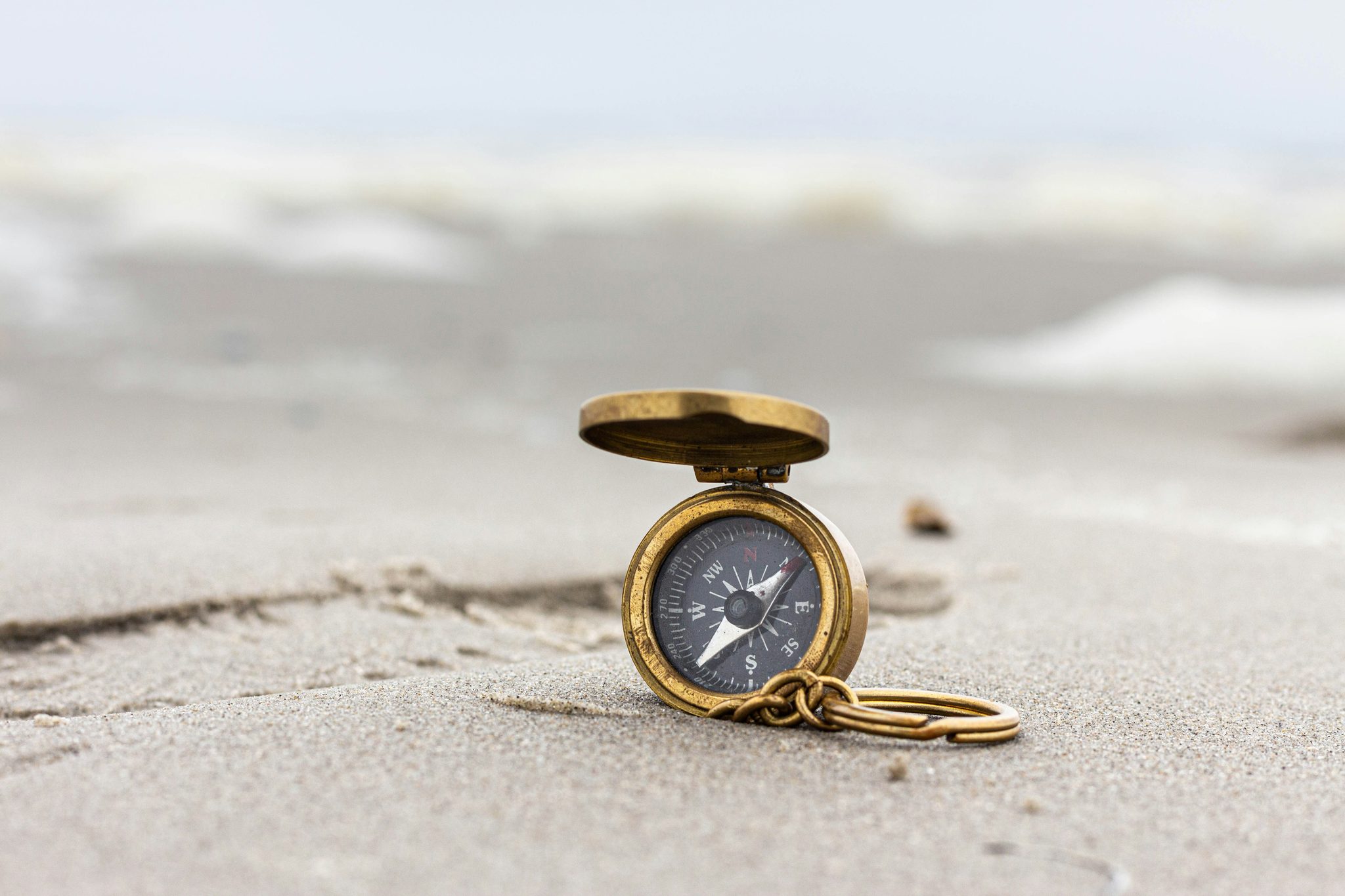 A brass compass lying in the sand at the edge of the sea