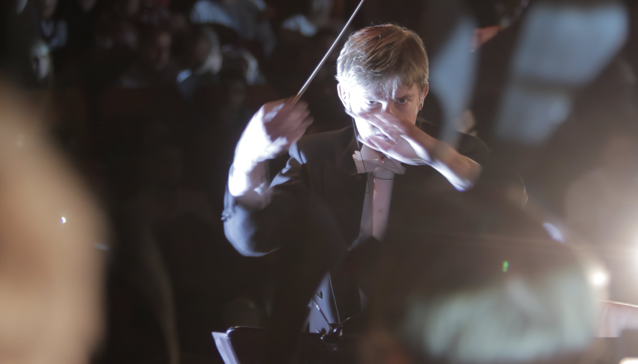 A conductor mid-gesture in front of an orchestra